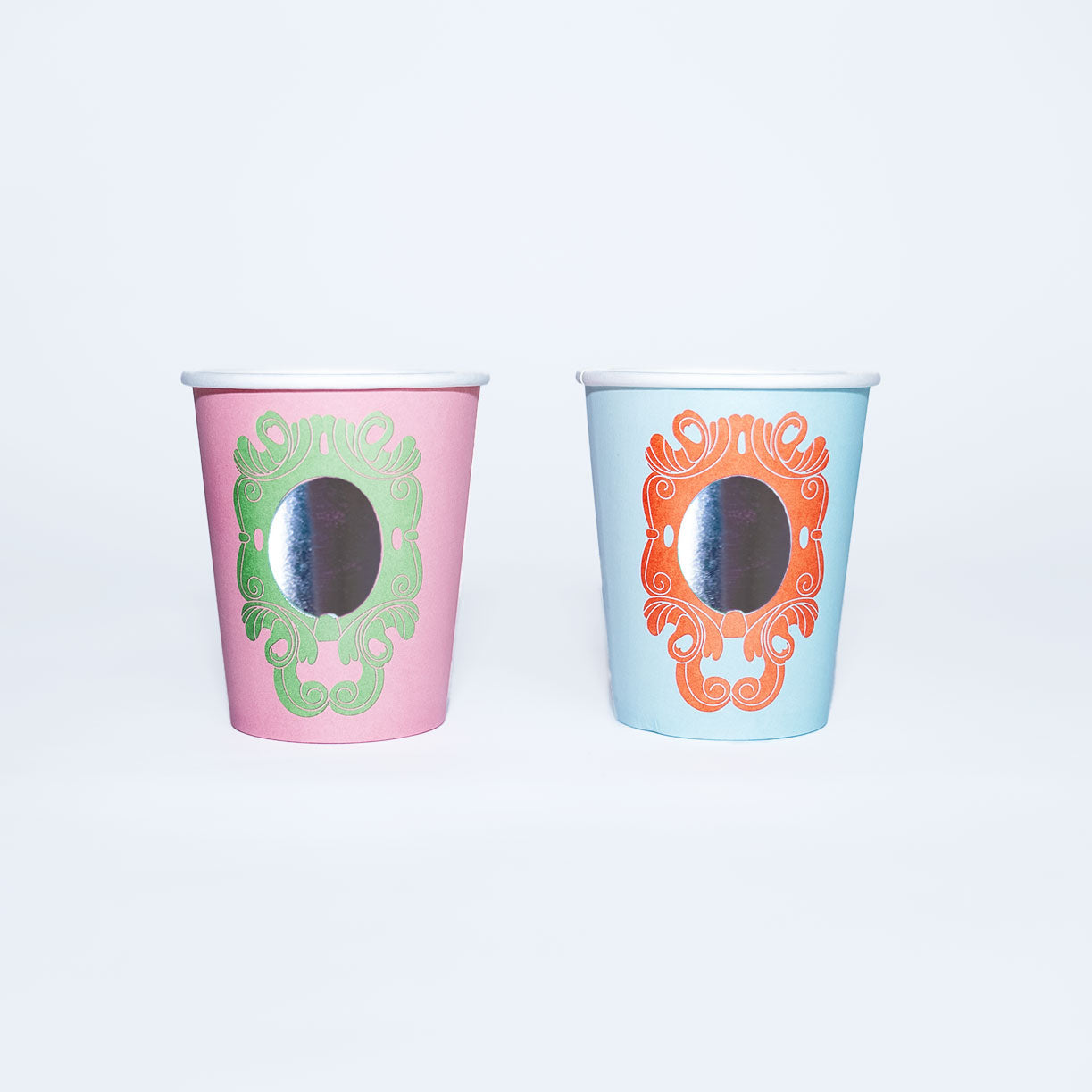 Two decorative princess party cups with mirror-like finishes, one pink with green design and one blue with orange design.