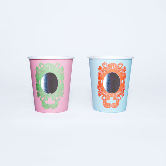 Two decorative princess party cups with mirror-like finishes, one pink with green design and one blue with orange design.