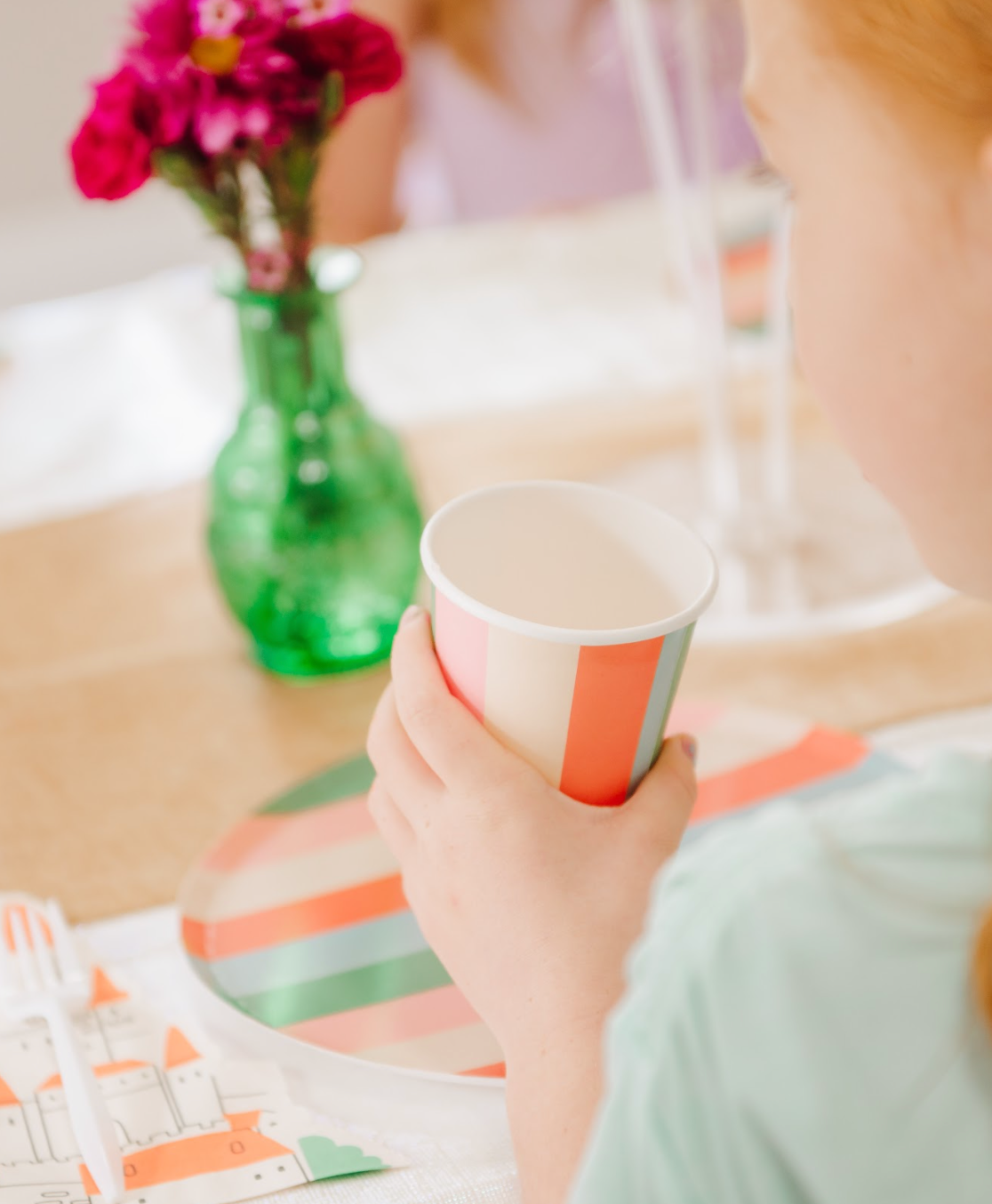 Child holding pastel striped paper cup at colorful party table setting