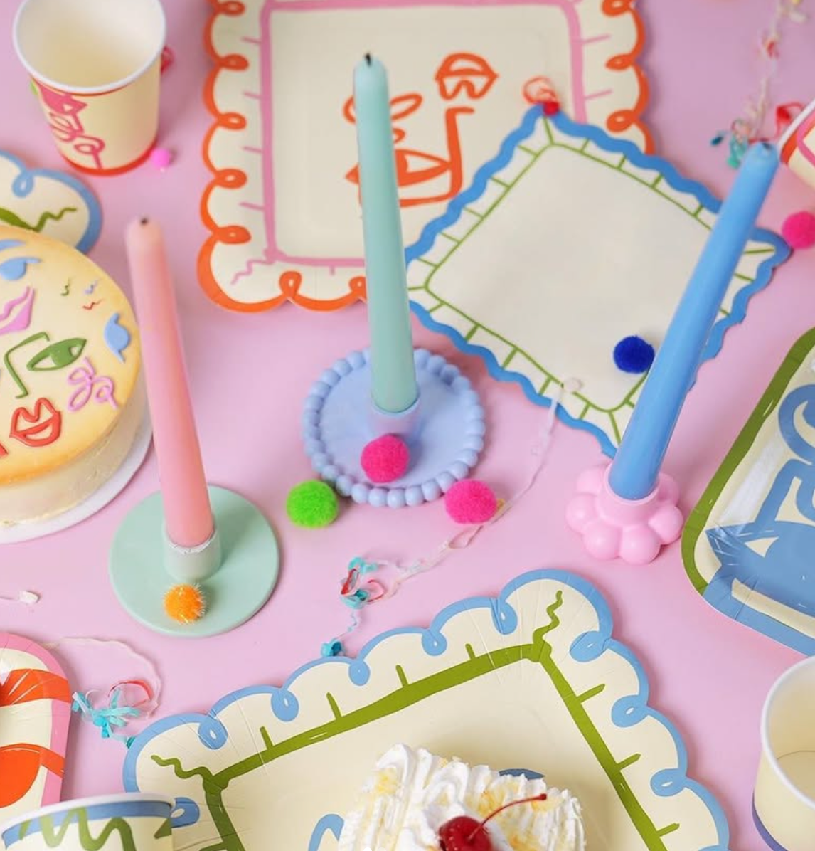 Colorful birthday party setup with candles, plates, and a cake on a pink tablecloth.